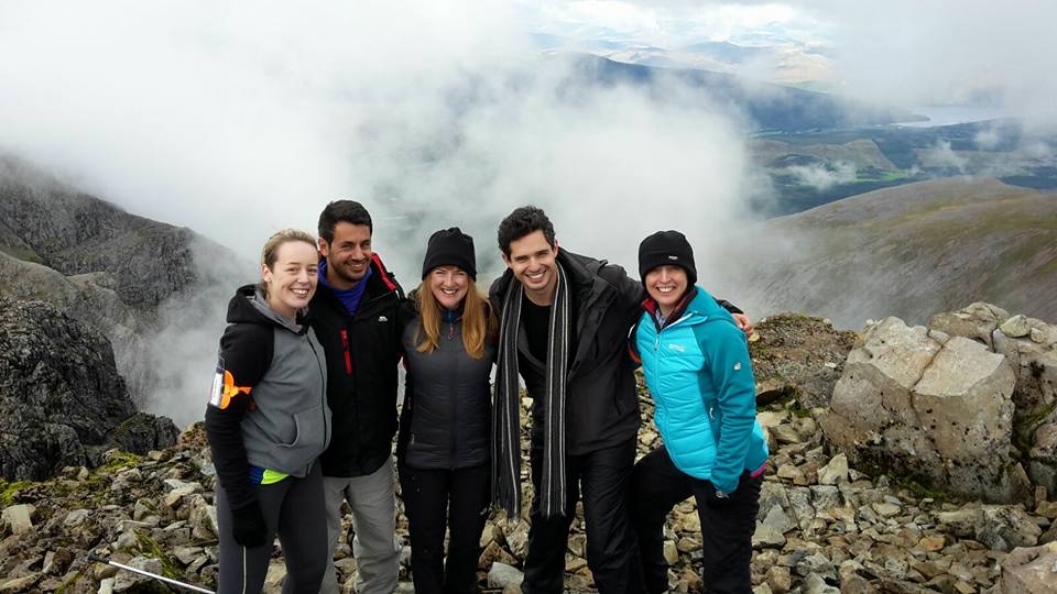 A group of people smiling while standing on top of a rocky hill