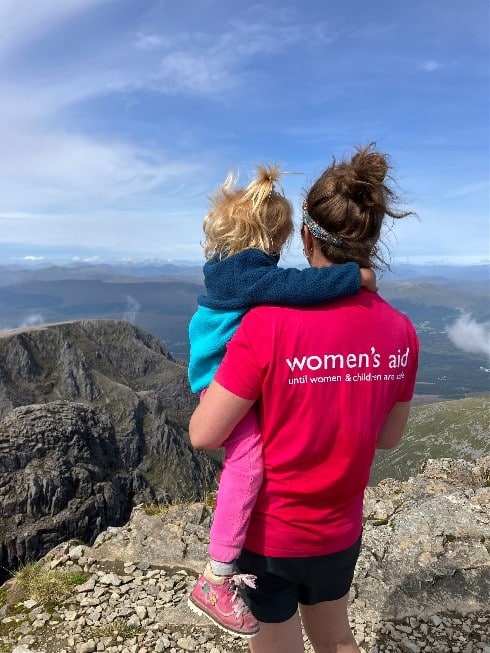 A woman holding her child at a viewpoint wearing a Women's Aid T-Shirt.