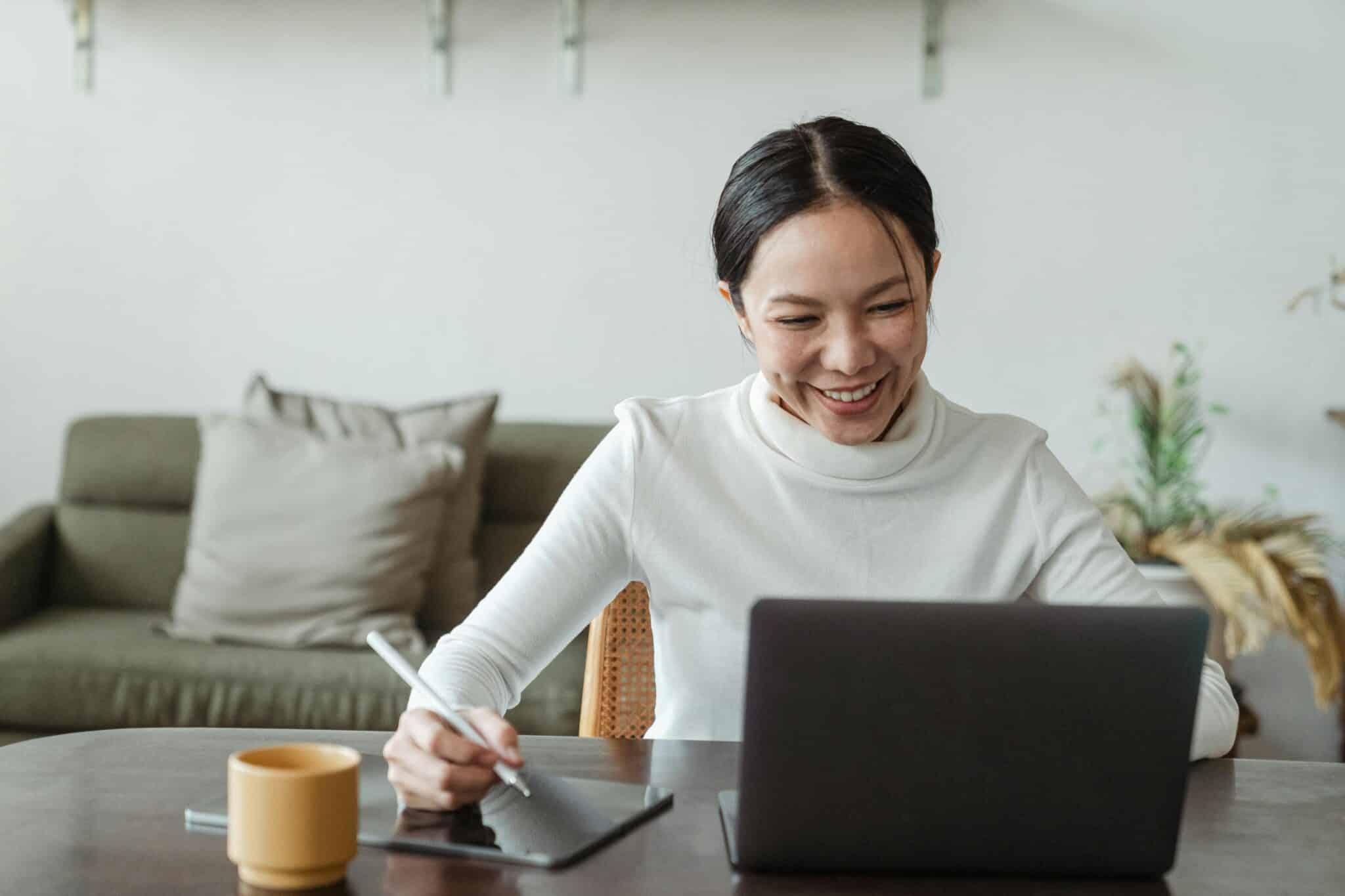 An image of a woman smiling while working on a laptop.
