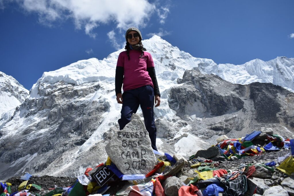 Woman standing in mountains behind a rick that says 'Everest Base Camp 2018'