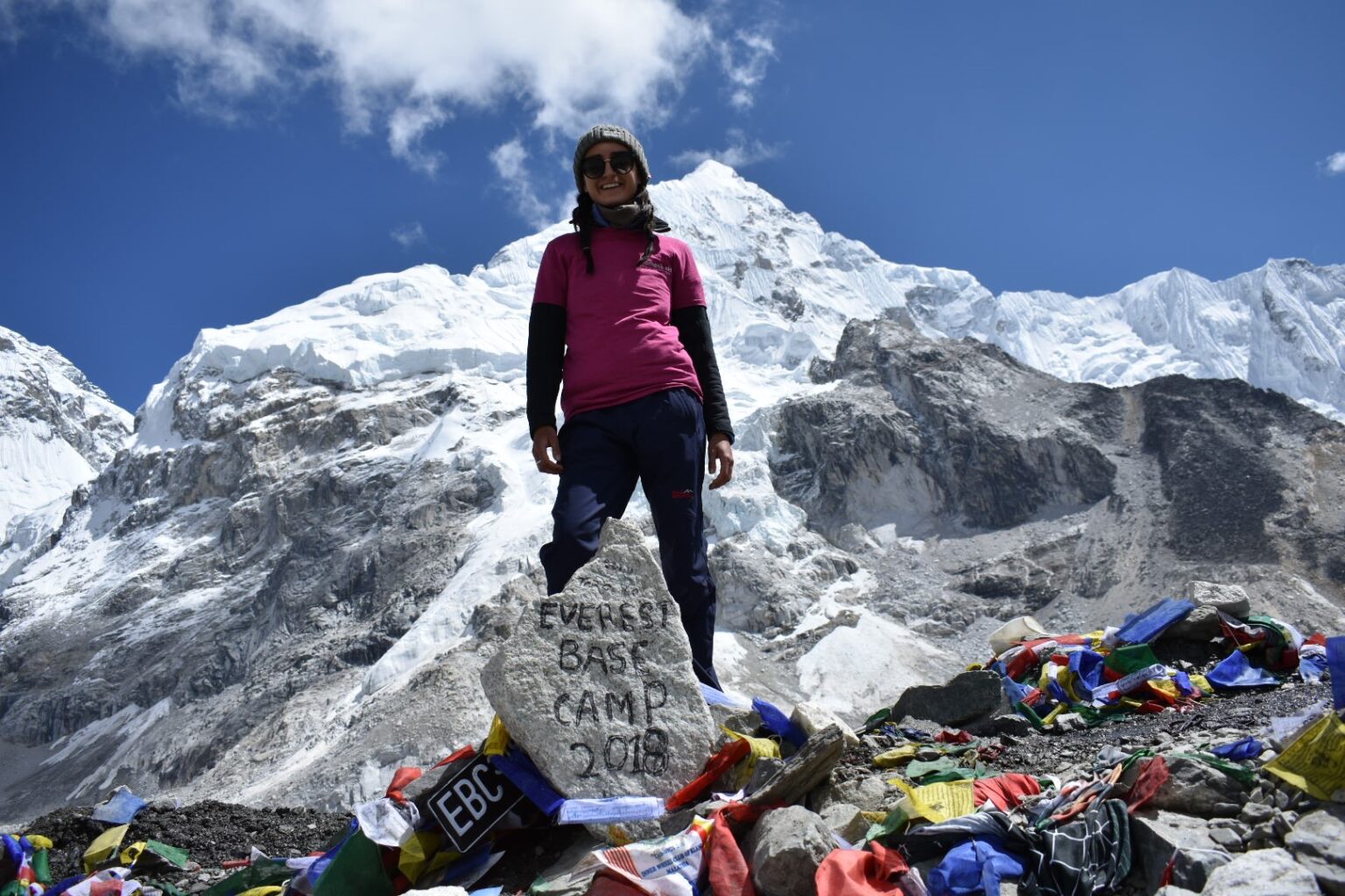 Woman standing in mountains behind a rick that says 'Everest Base Camp 2018'