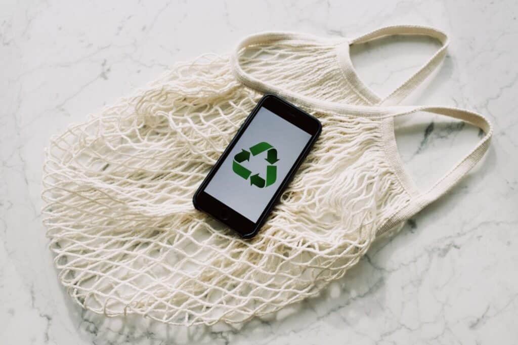 Mobile phone with recycling logo on screen, sitting on top of a mesh cream bag