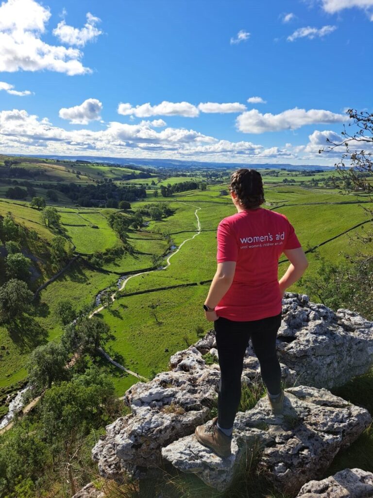 Woman wearing Women's Aid t-shirt standing on top of a rocky hill looking out into the distance