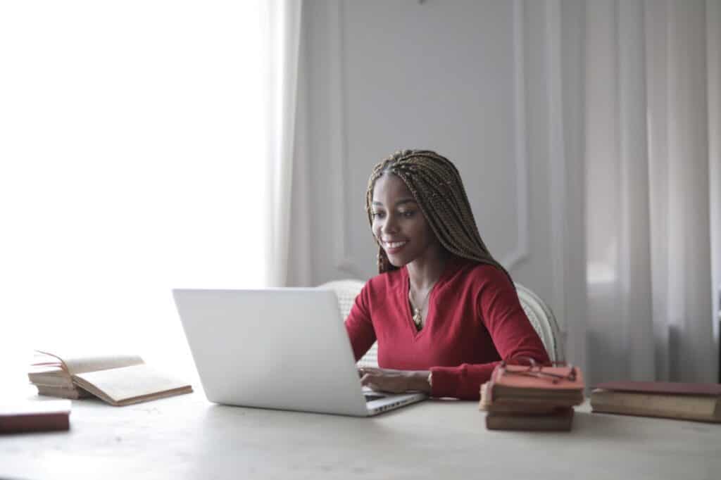 Woman smiling while sitting at a desk surrounded by books and looking at a laptop