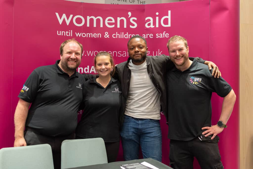 A group of people smiling standing in front of a Women's Aid banner