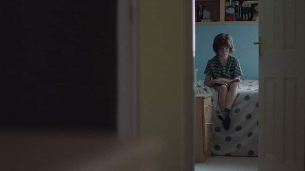 A child sitting in a room with the door ajar
